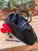 Black woven handbag on a stone surface with red flowers and a pen nearby